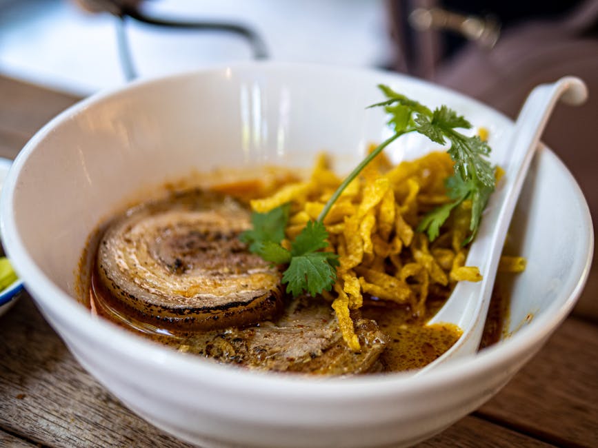 A bowl of Khao Soi with crispy and soft egg noodles in a spicy curry soup, topped with chicken and garnishes